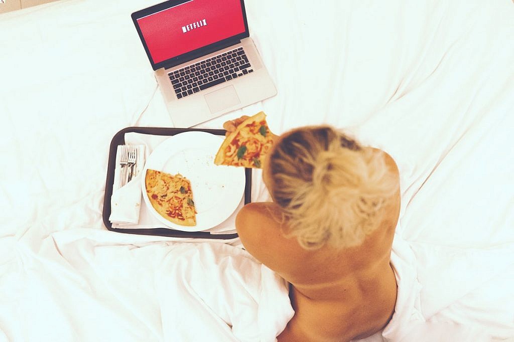 Kobieta leżąca i oglądająca Netflixa jedząc pizze - Który pakiet wybrać?